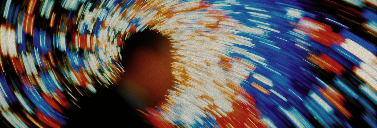 Blurred silhouette of a person against a swirling, colorful background of blue, red, white, and orange streaks creating a dynamic, motion effect.