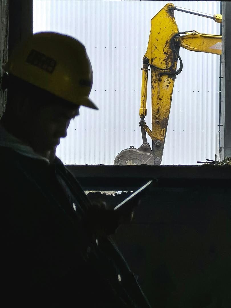 Technician in a hard hat working hands-on at a machine, representing guided assembly and maintenance on a factory floor