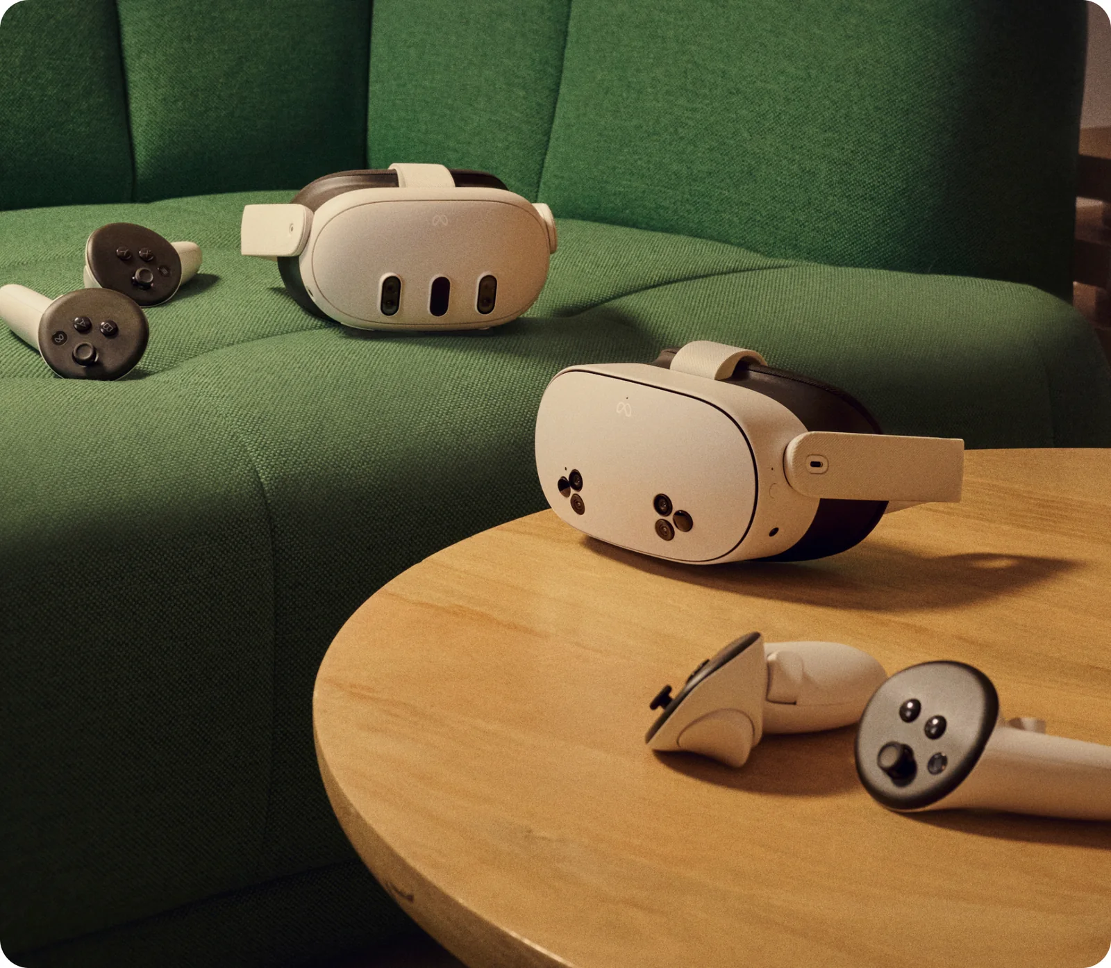Two Meta Quest headsets and two pairs of Touch Plus controllers, one set resting on a green sofa and the other on a round wooden table