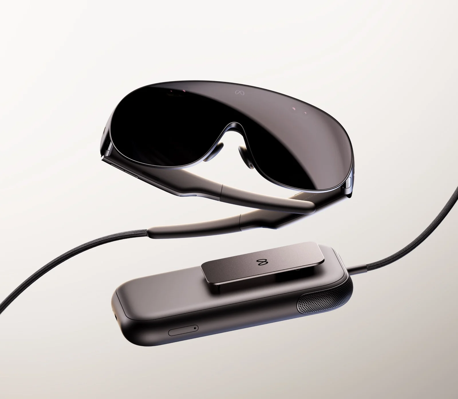 Meta VR Glasses shown at an angle above their tethered compute puck, a dark wraparound visor on thin temple arms with a braided cable running from the left arm to a rounded rectangular puck with a clip on its back