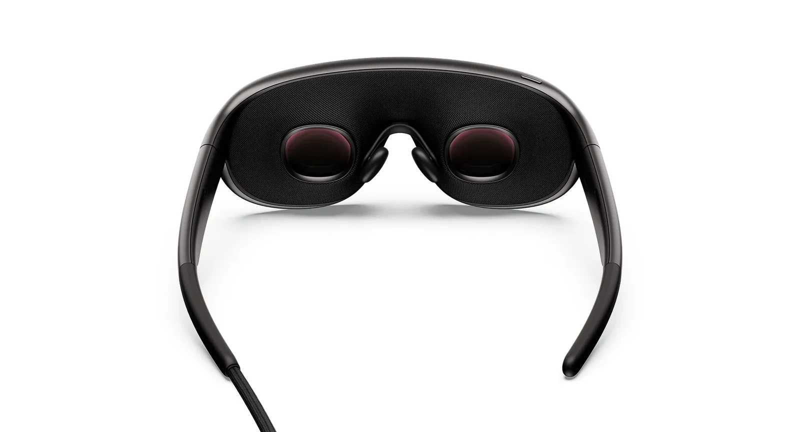 Inside view of Meta VR Glasses on a white background, showing two small round pancake lenses with a reddish sheen set in a dark light-blocking gasket, the adjustable nose pads between them and the tether leaving the left arm