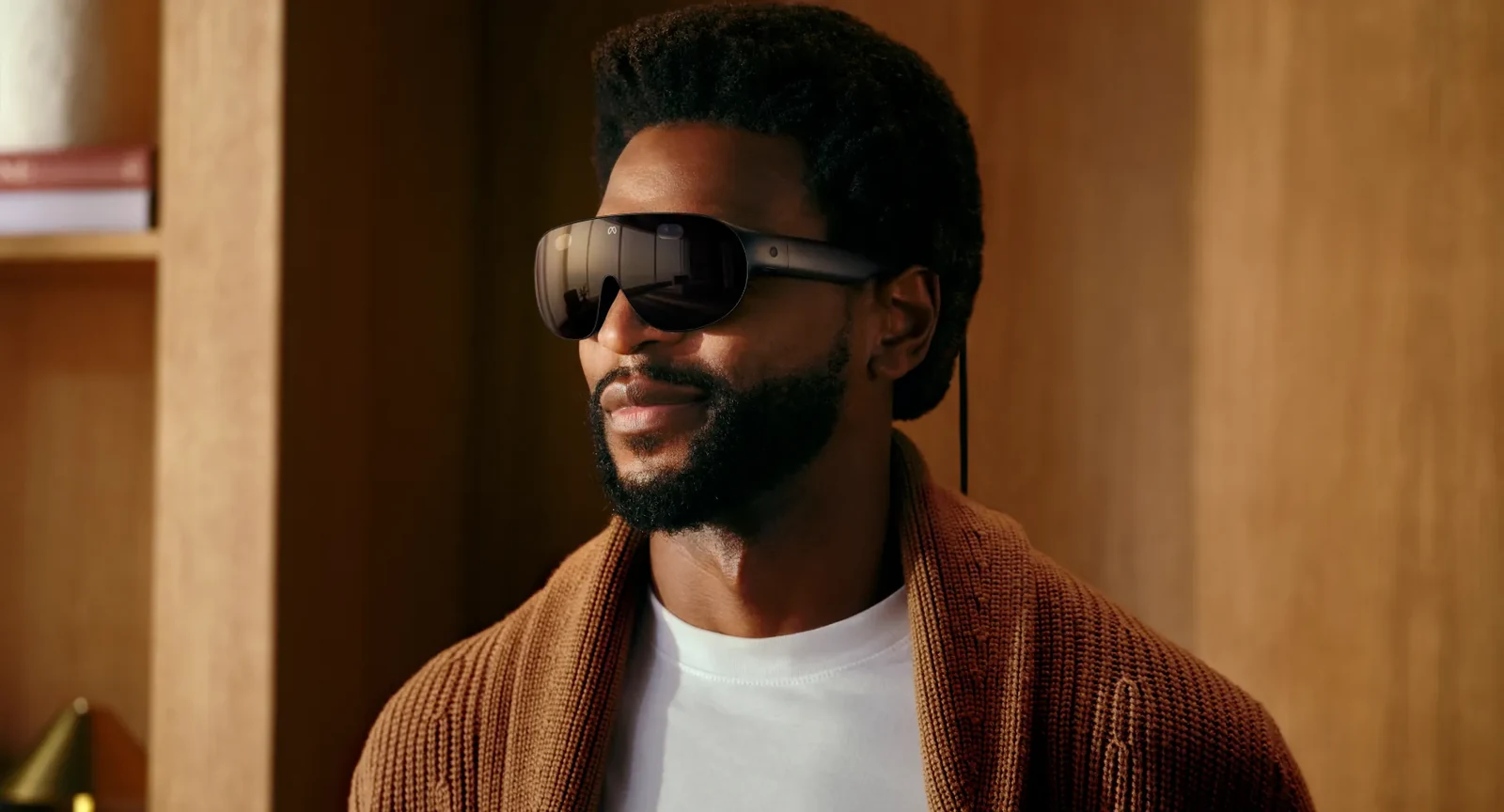A person wearing Meta VR Glasses indoors, seen from the side, with the open sides of the visor visible and the tether running down from the temple arm