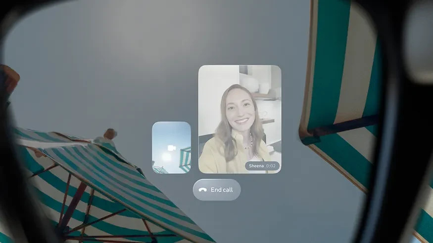 Meta's rendering of the view through Meta Ray-Ban Display, a video call panel showing a caller's face and an End call button floating over a striped beach umbrella, framed by the edge of the lens