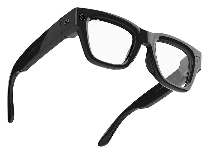 Meta Ray-Ban Display glasses at an angle on white, a thick black frame with clear lenses, a camera in one outer corner and a small Meta logo on the temple arm