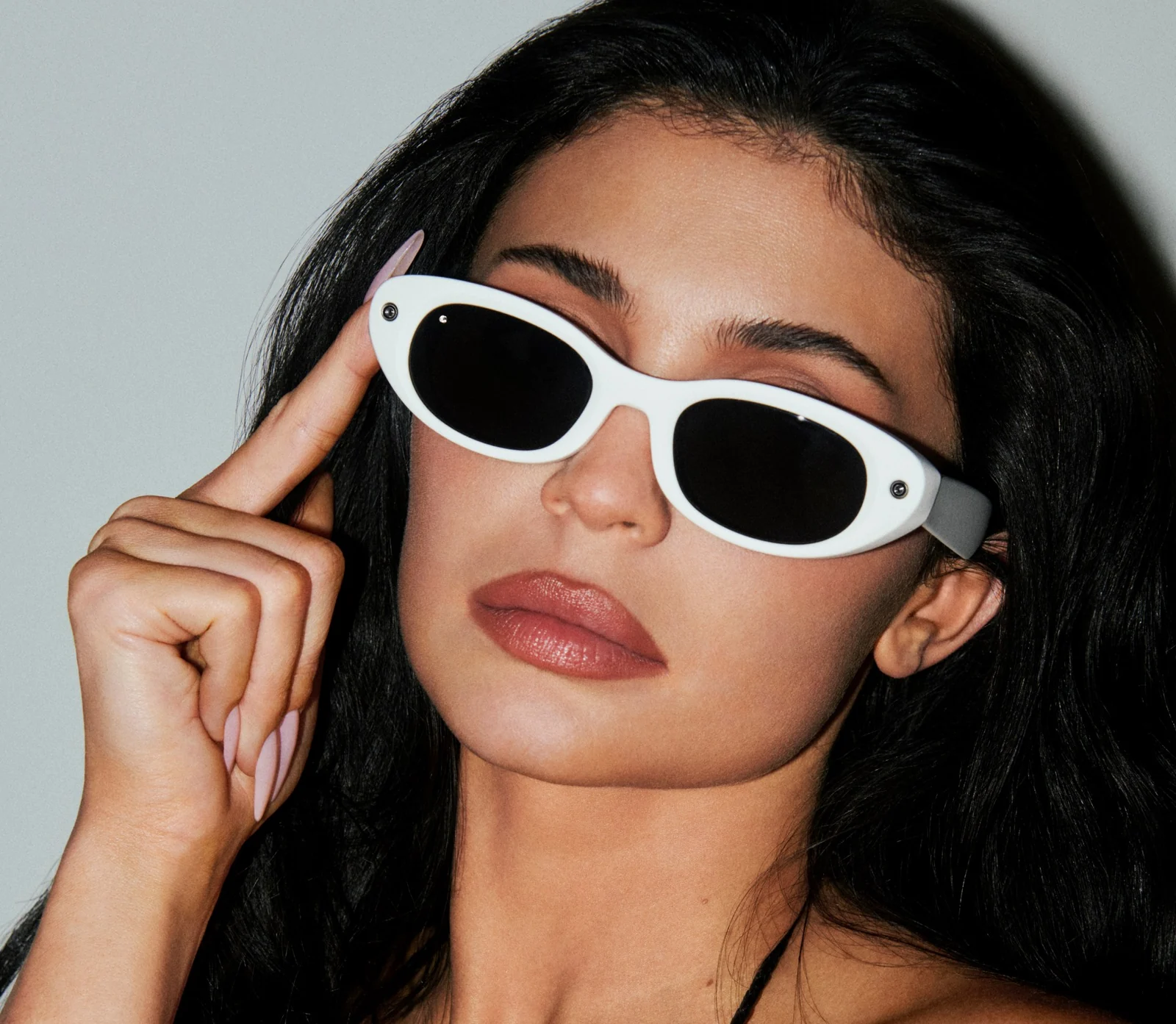 A person wearing the Ivory colorway of the Meta Glasses Starfire, a white oval frame with dark lenses, a camera at one outer corner and an LED at the other