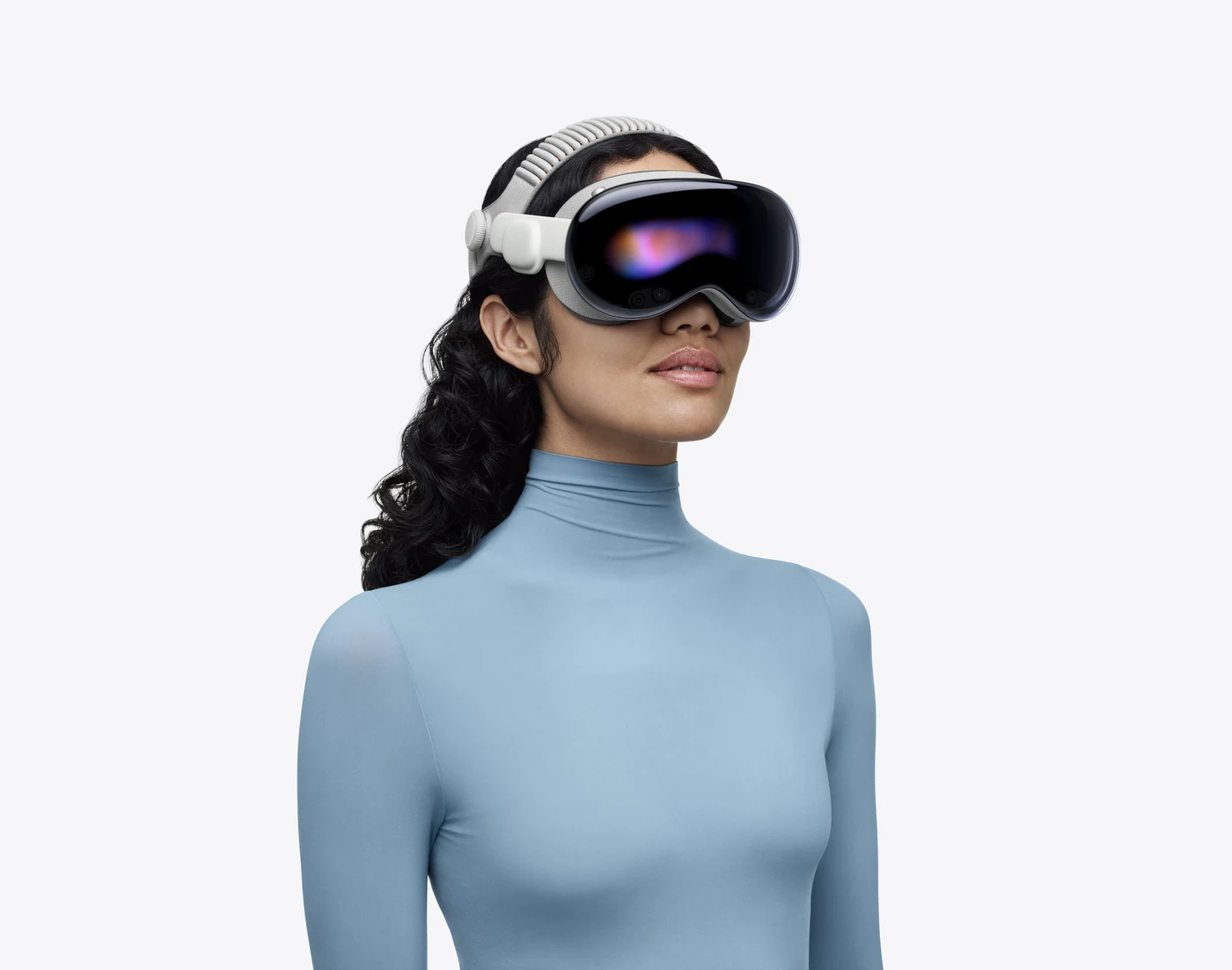 A person wearing Apple Vision Pro with the Dual Knit Band, seen from the chest up against a pale background, the curved glass front reflecting blue and violet