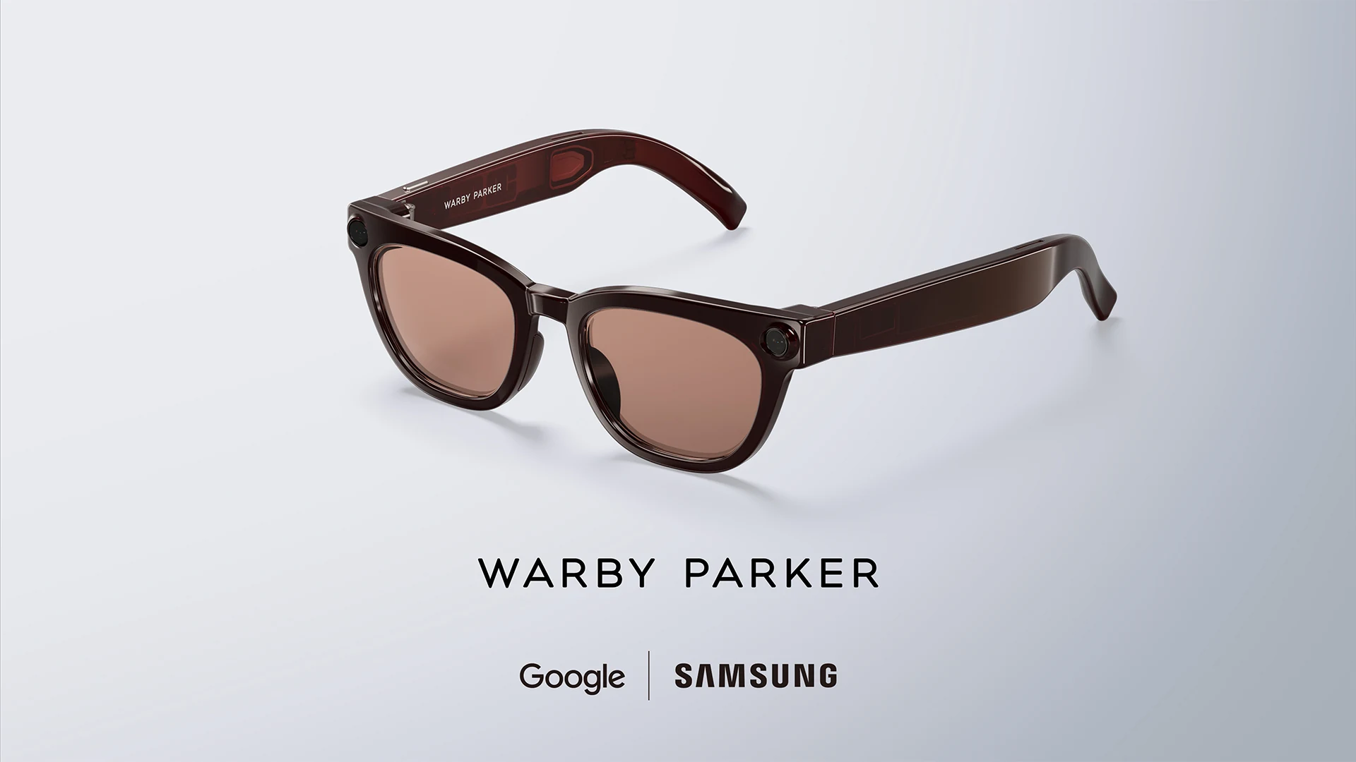 Samsung intelligent eyewear in a dark red Warby Parker frame, photographed at three quarters on a pale grey background with the temple arms open, a small round module at each outer hinge and Warby Parker above Google and Samsung logos beneath