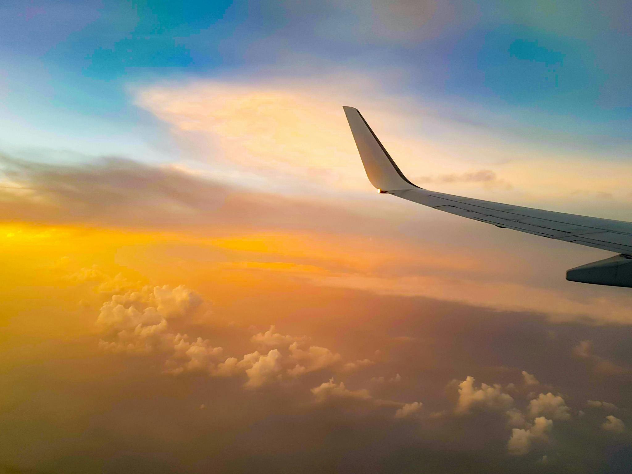 Airplane wing above the clouds at sunset, representing managed corporate travel