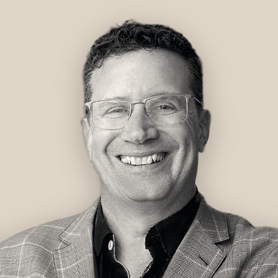 Nathan Cockerill, smiling in a checked jacket, black-and-white on a warm sand background