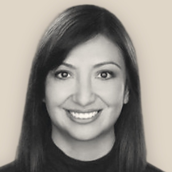 Jeannette Flynn, smiling in a black top, black-and-white on a warm sand background