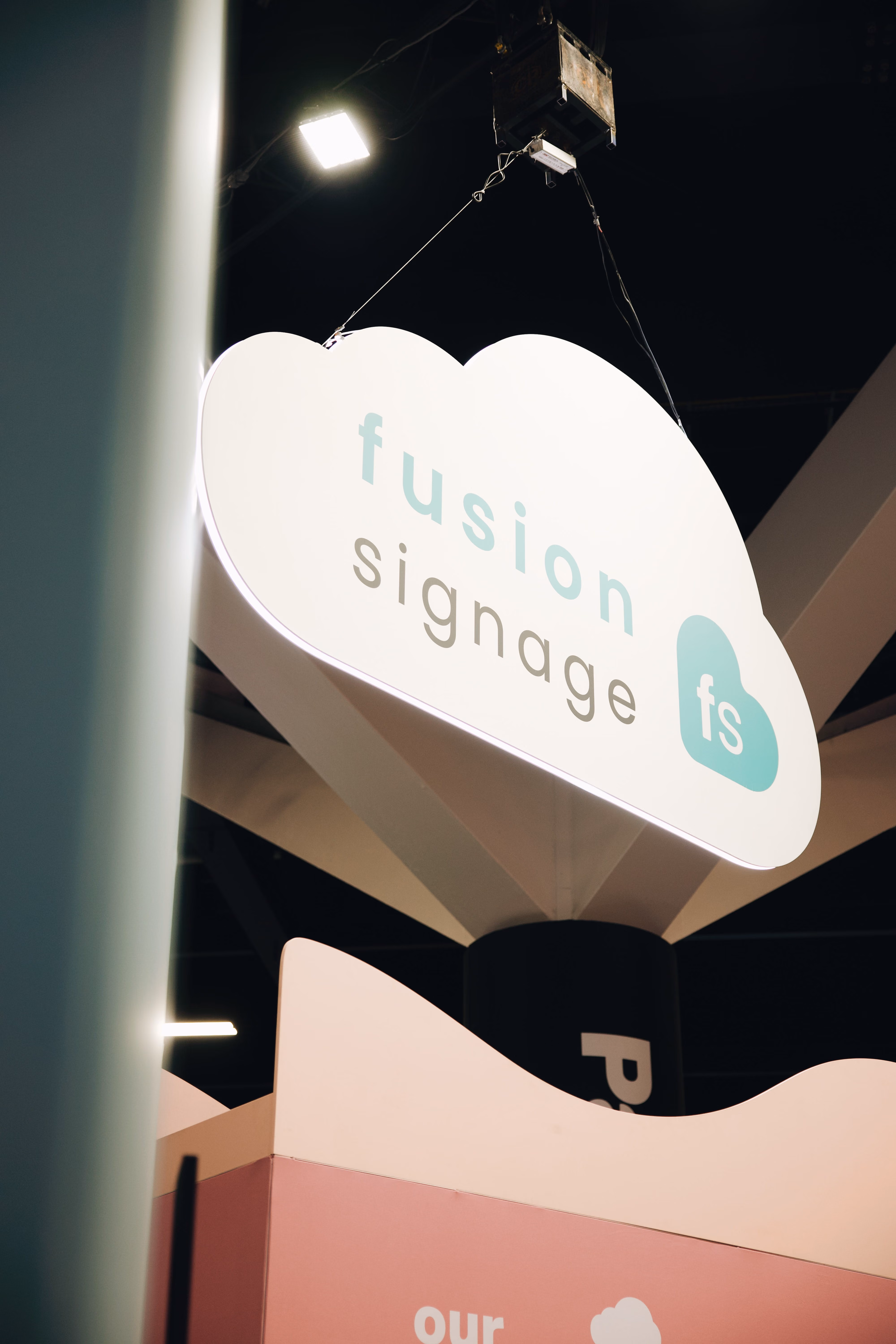 White cloud-shaped sign hanging indoors with text 'fusion signage' and blue 'fs' logo.