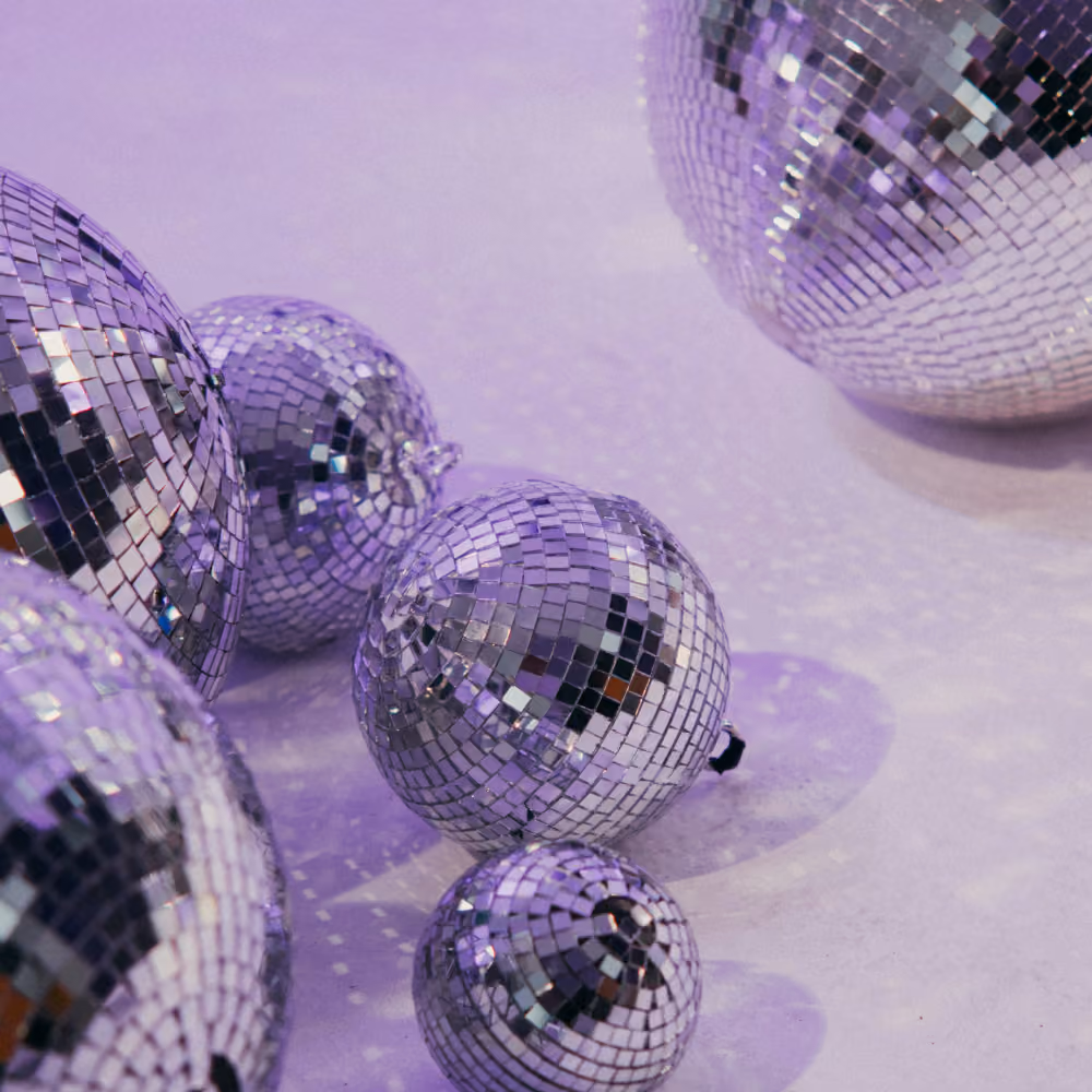Several reflective disco balls of varying sizes on a purple-lit surface casting light patterns.