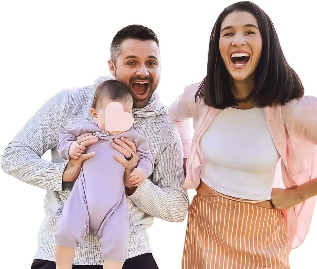 Smiling man holding baby and happy woman standing beside them against white background.