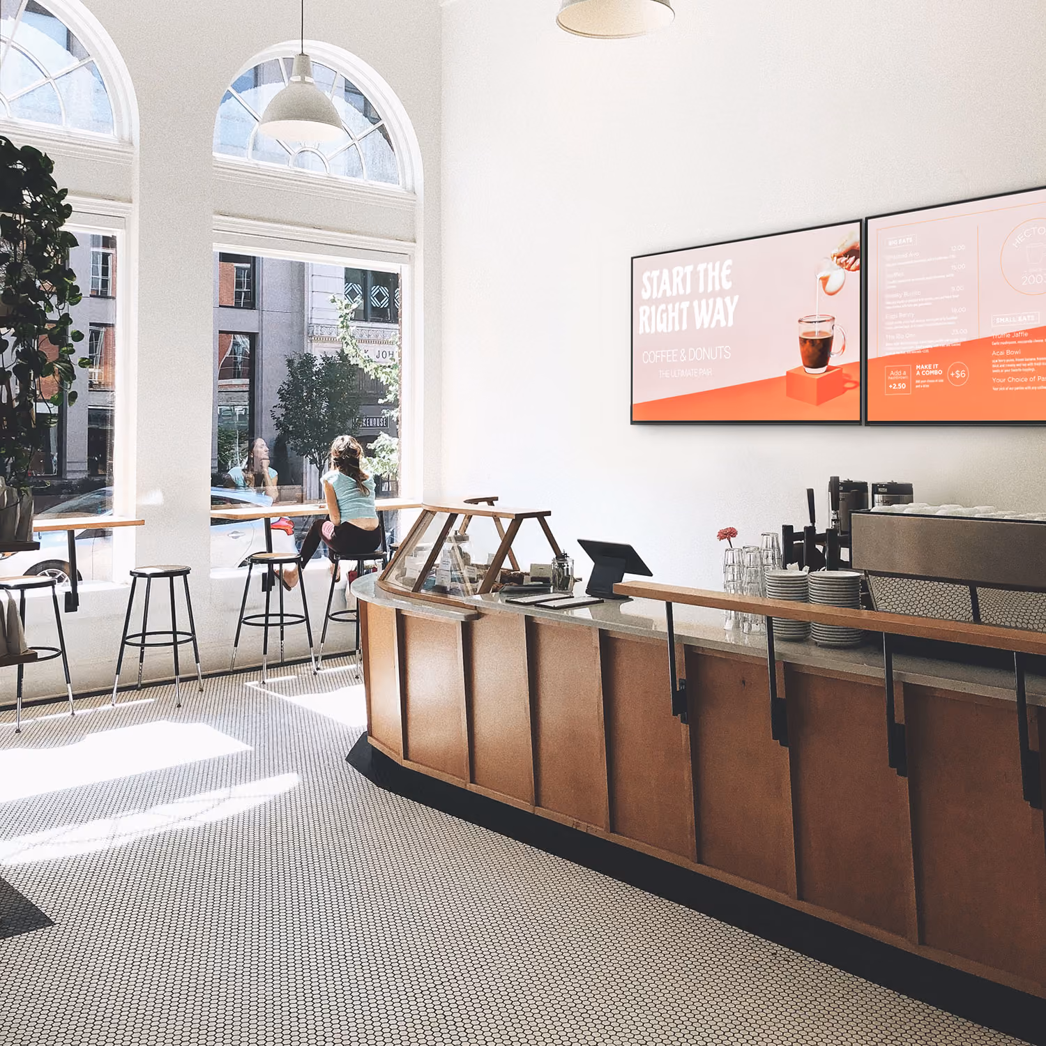 Bright coffee shop interior with a woman at window seating and a menu board reading 'Start the right way'.