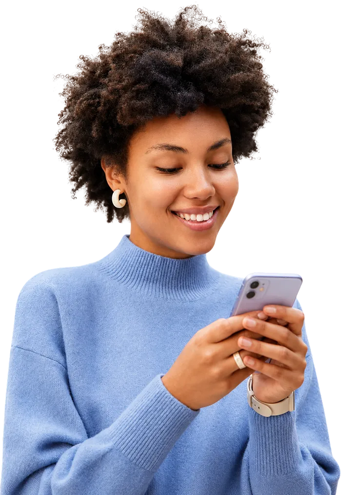 Smiling woman with curly hair wearing a blue sweater, looking at her smartphone.