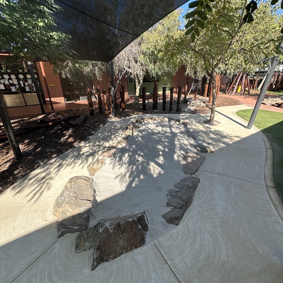 Sandpit with natural log features under shade at an early learning centre