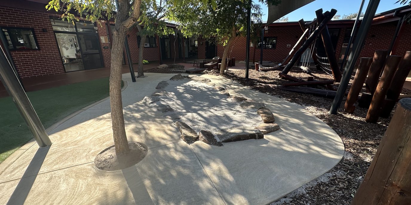 Early learning centre play yard with shade sail, trees and sand play area