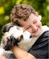 Smiling young boy hugs a fluffy black, white, and brown dog.