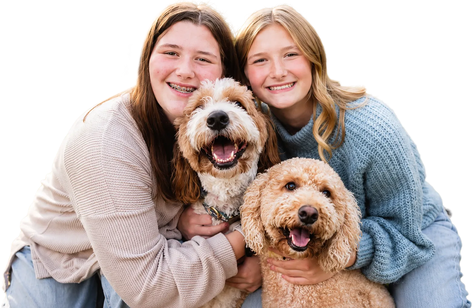 Two smiling girls with braces pose closely together, each hugging a happy, curly-haired dog.