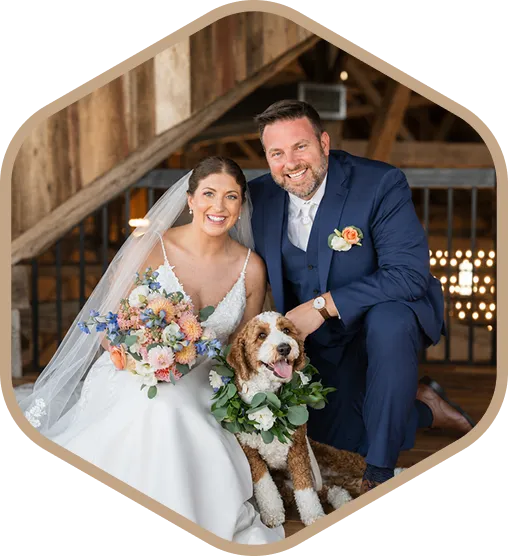 Bride and groom smiling and posing with a Mountain Doodle dog wearing a floral wreath.