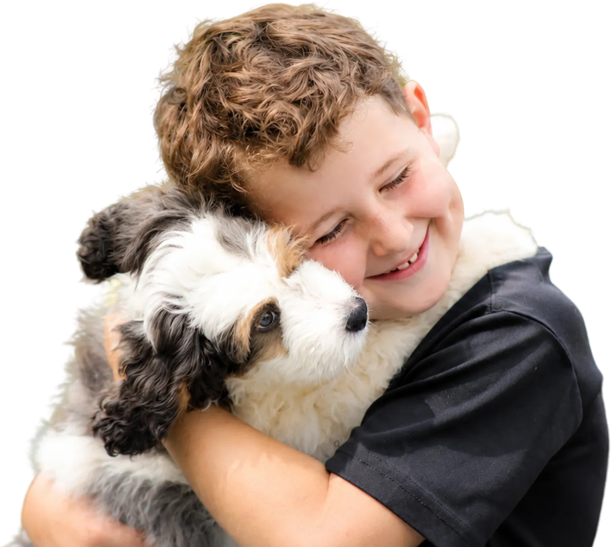 Smiling boy hugging a fluffy black, white, and brown puppy.