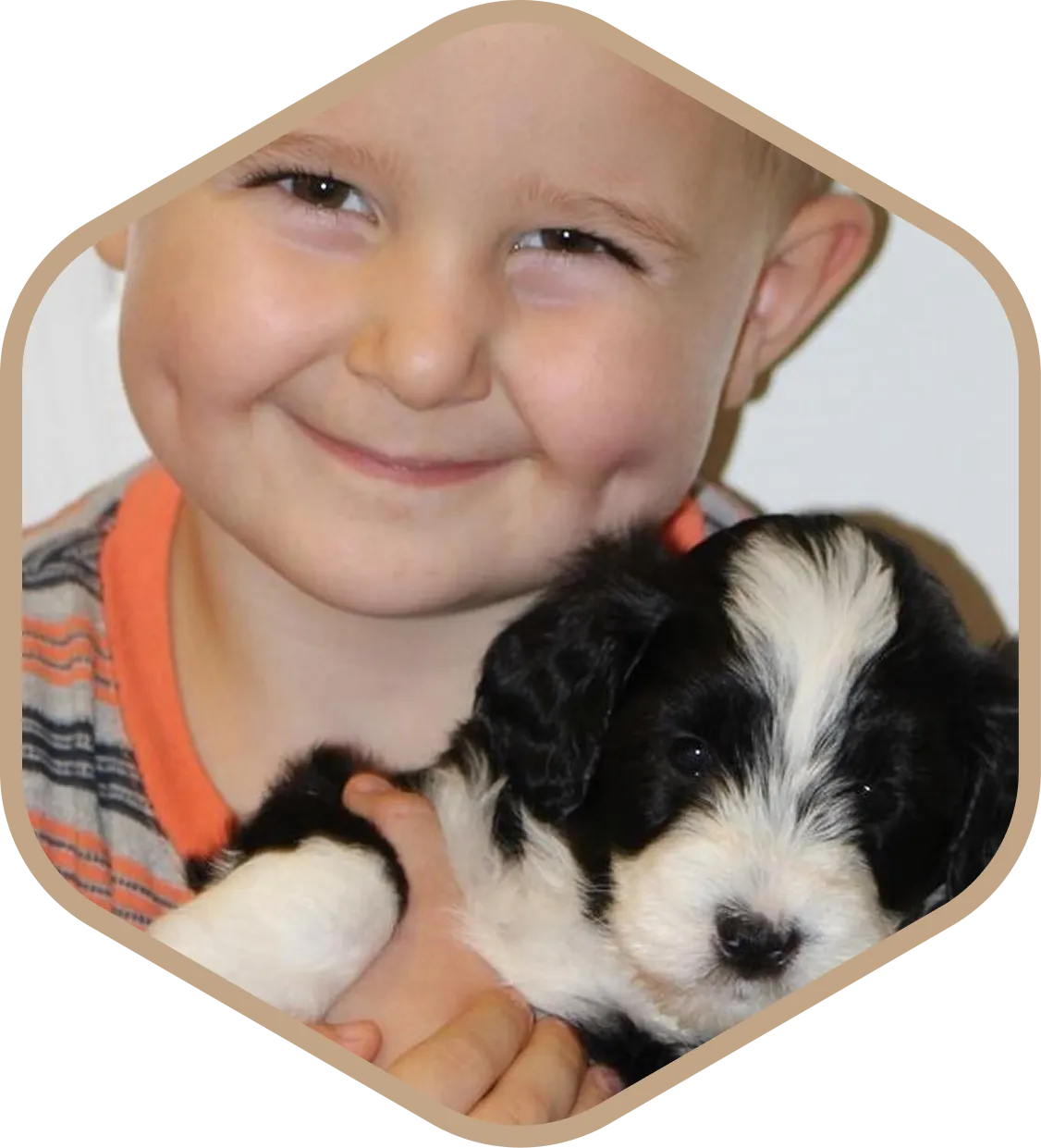 Smiling child with dimples holds a black and white puppy close to their face, both looking toward the camera.
