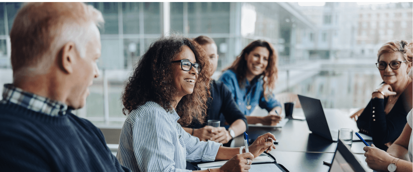 Colleagues smiling and talking around a table in a modern office meeting room
