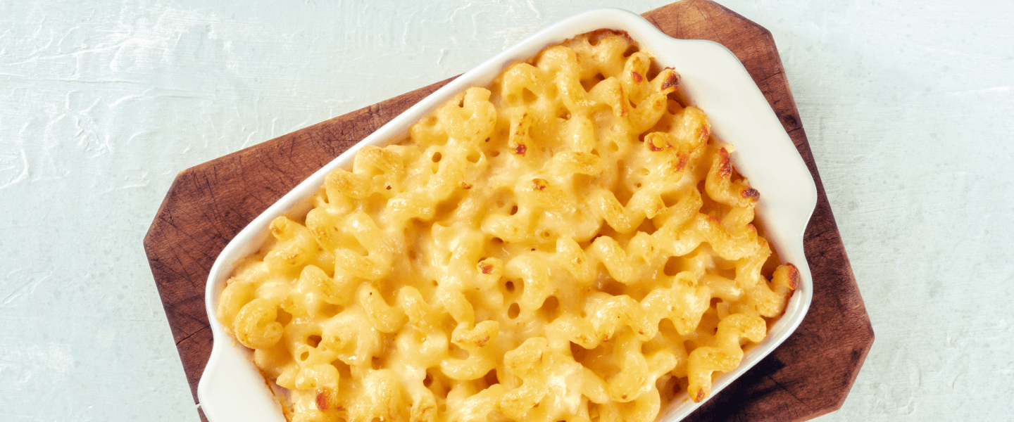 Baked macaroni and cheese casserole in a white dish on a wooden board