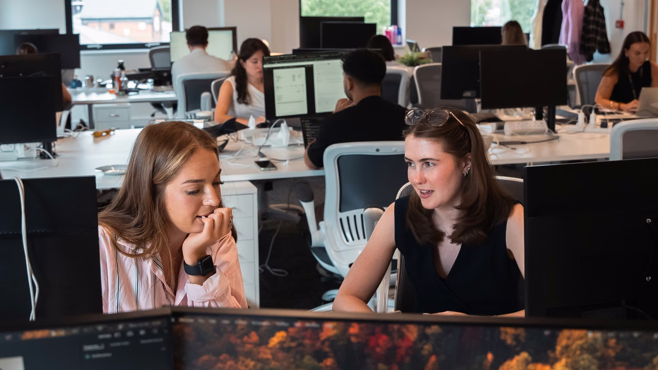 Two Campfire team members discussing work at their desks