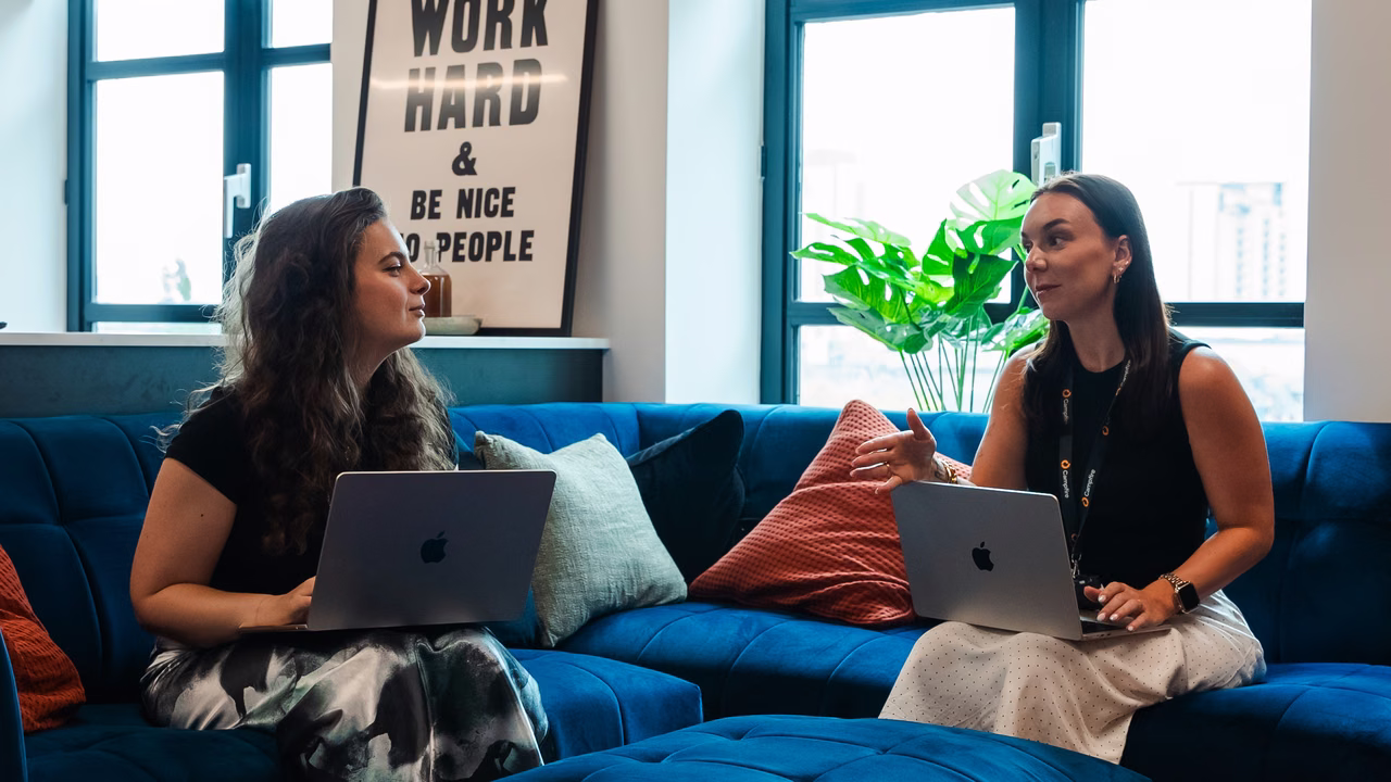 Two Campfire team members talking on a sofa with laptops in the office