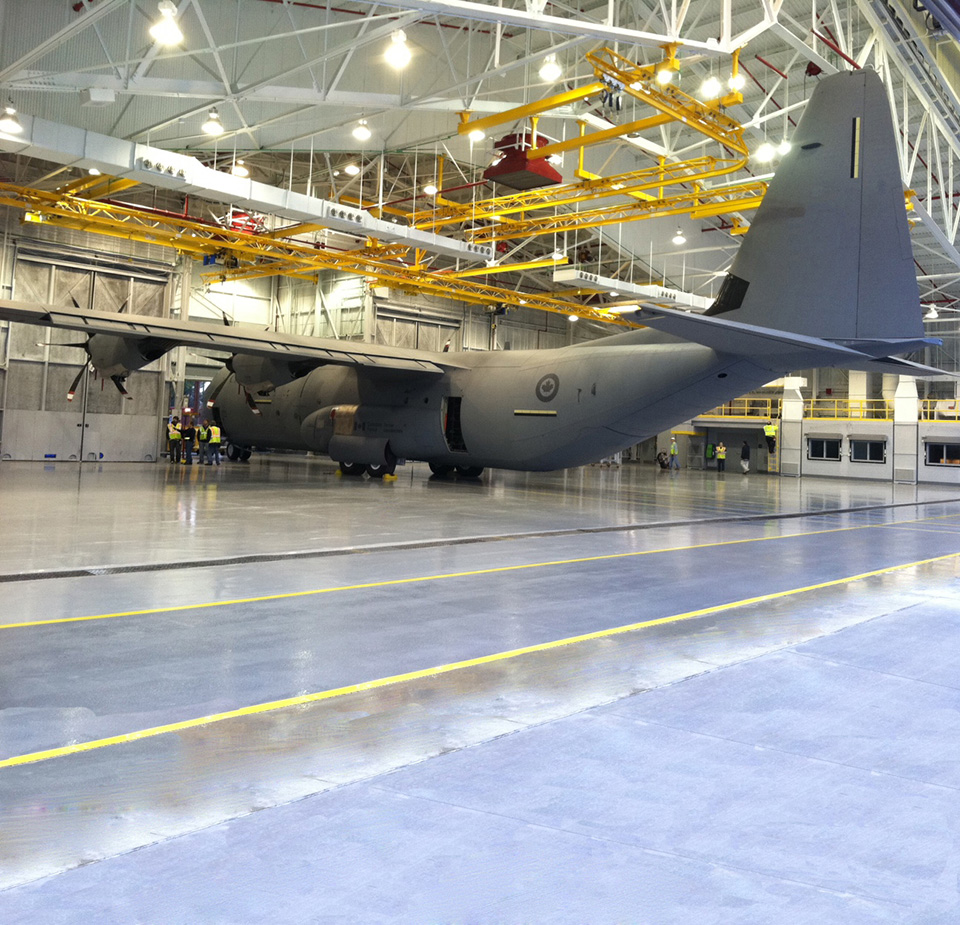 Lockheed Martin hangar with C-130 aircraft under a steel truss roof with overhead utility gantries