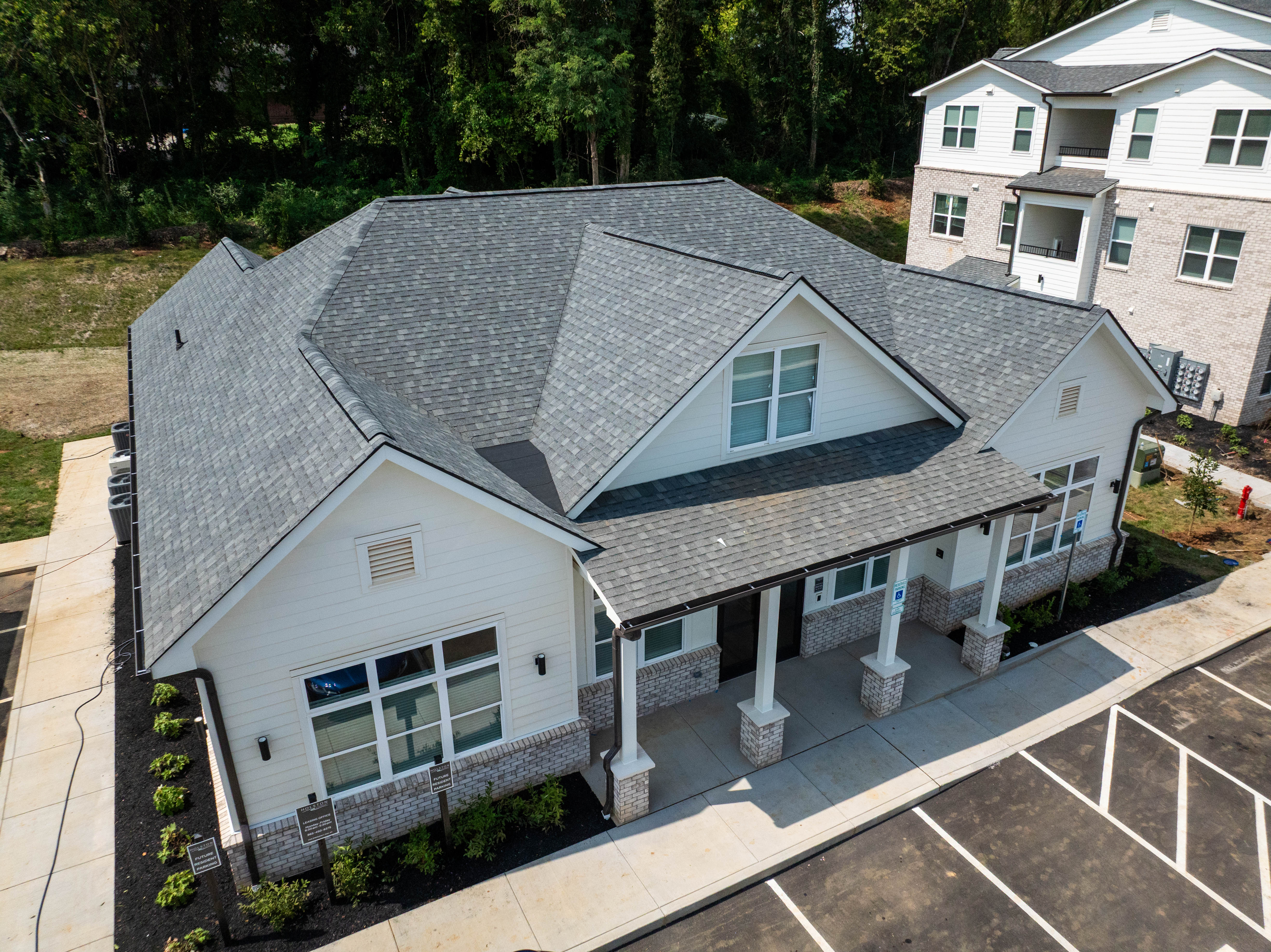 Aerial view of a multifamily clubhouse with gray shingle roof, covered porch and a nearby apartment building