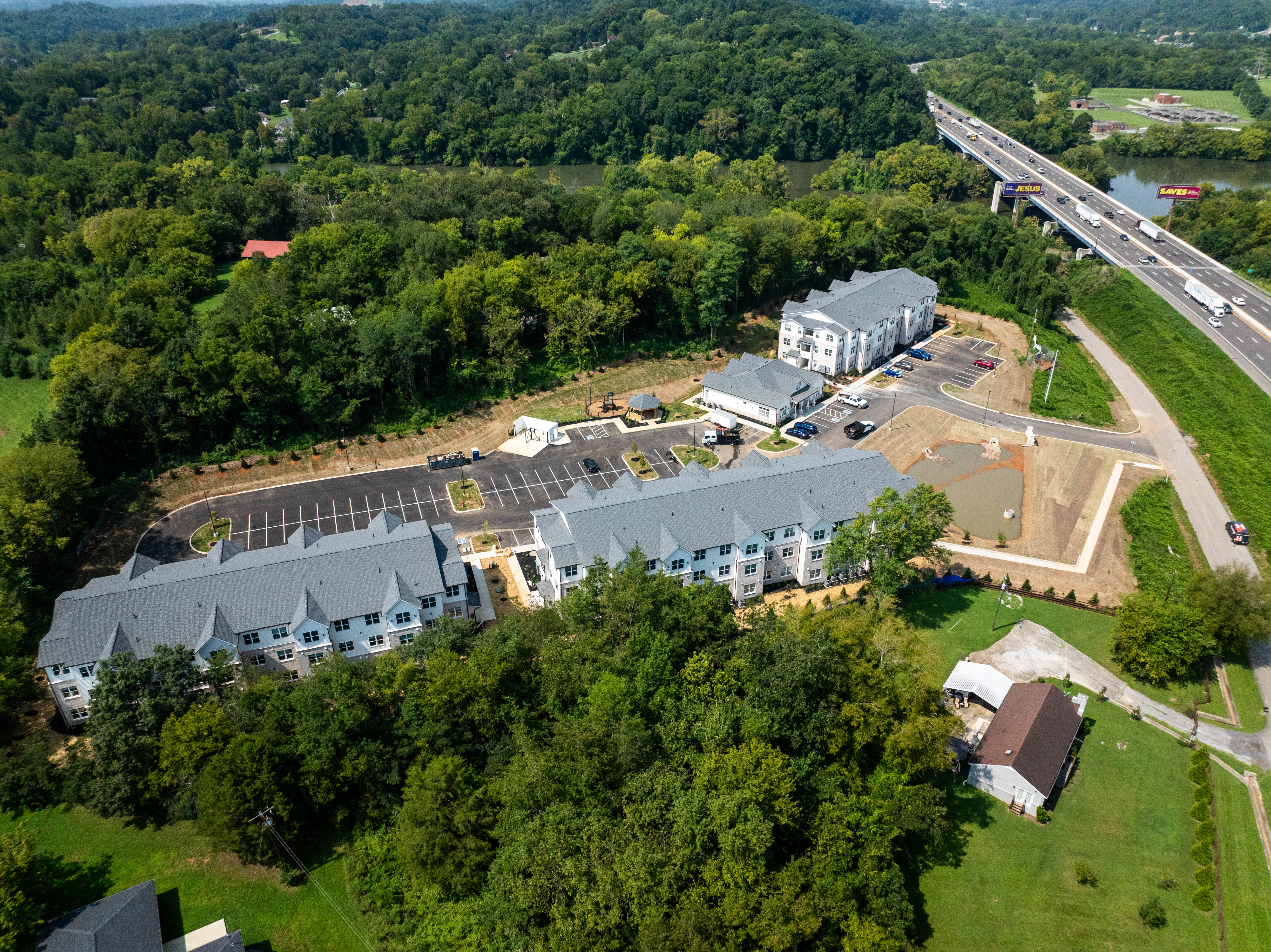 Aerial view of an apartment community with parking lot and clubhouse beside a river and interstate