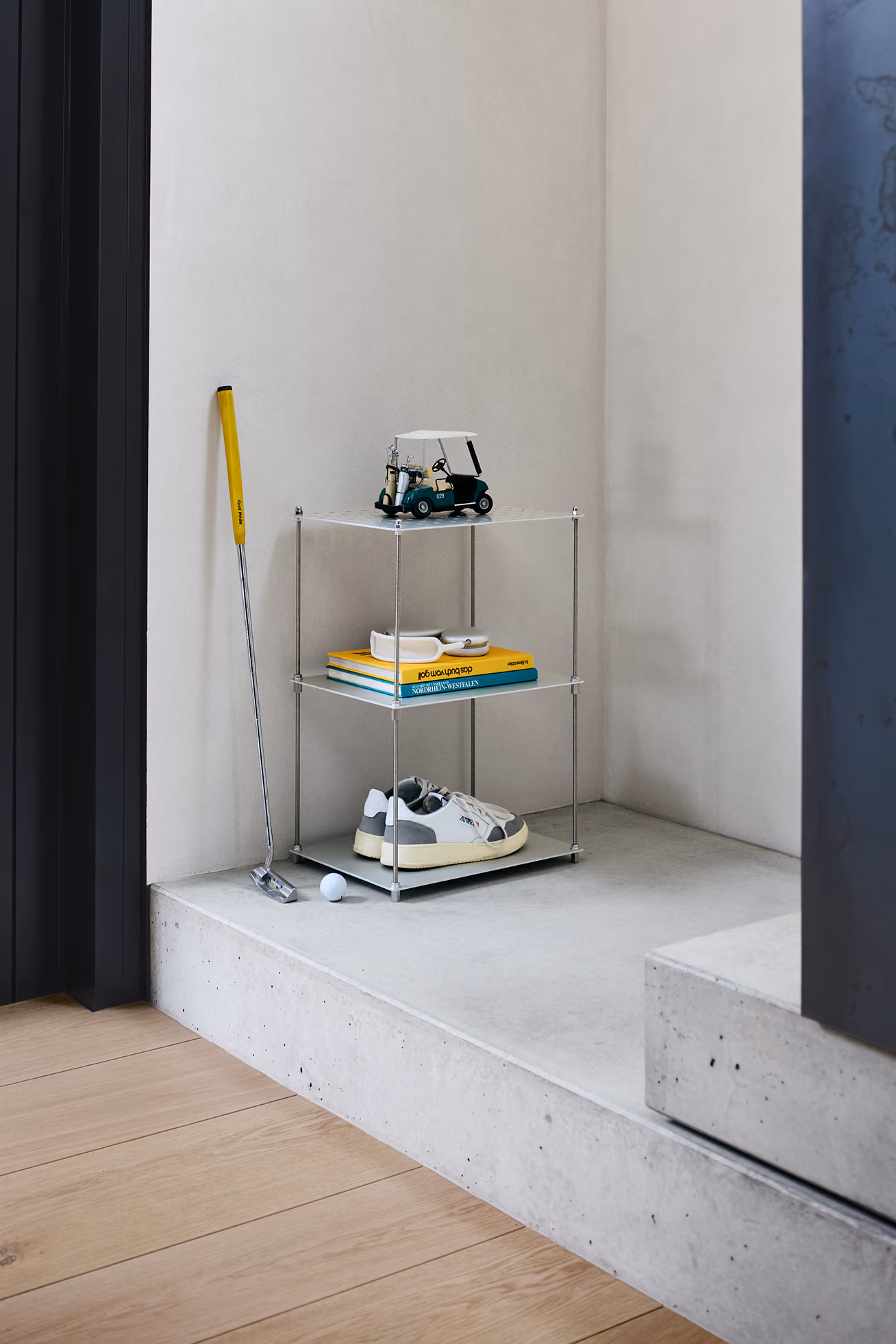 Golfschläger mit gelbem Griff lehnt an Wand, neben einem Regal mit Modell-Golfwagen, Schuhen und Büchern.