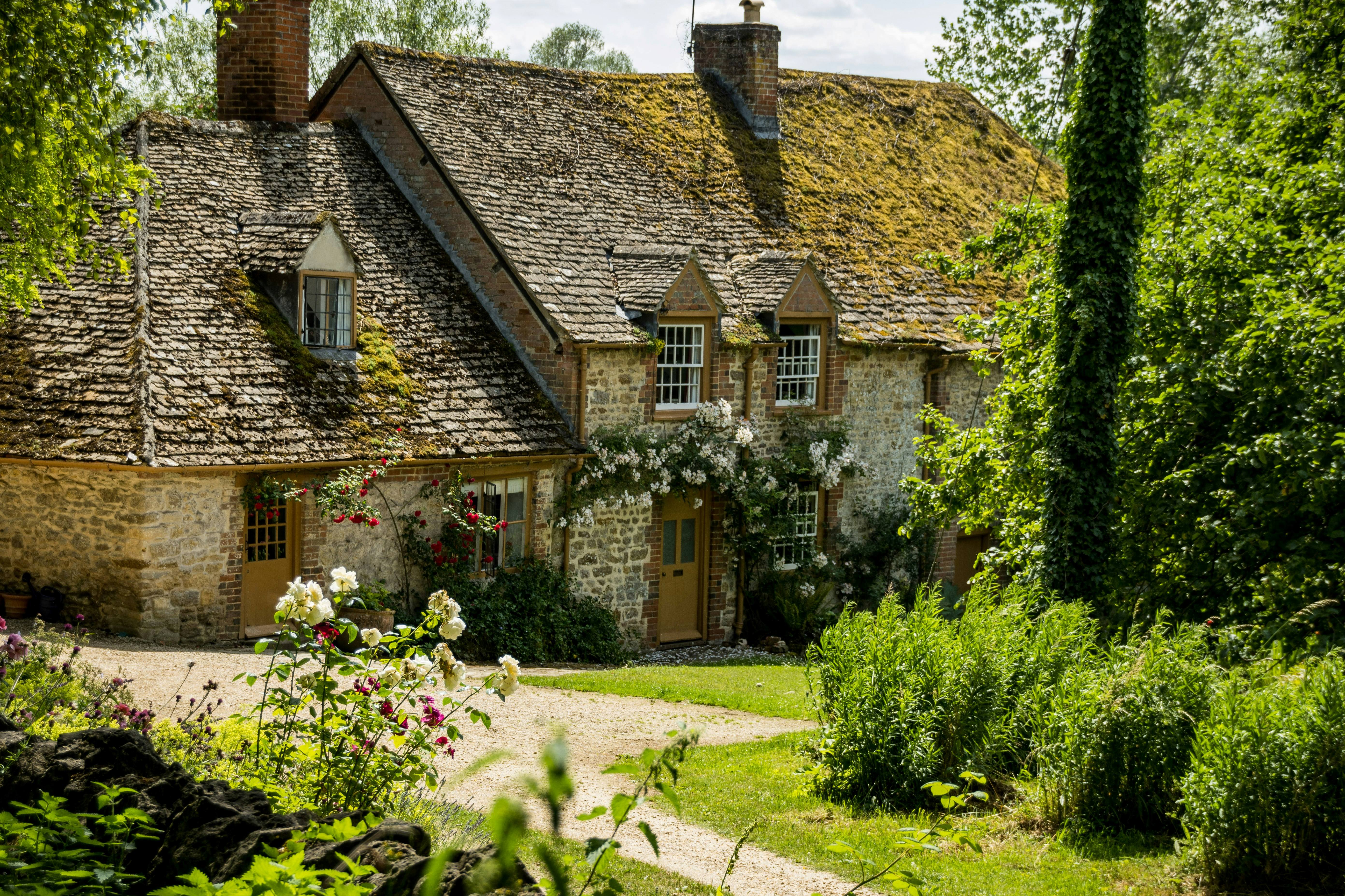 Traditional stone cottage with stone-tiled roofs, climbing plants and a mature garden.