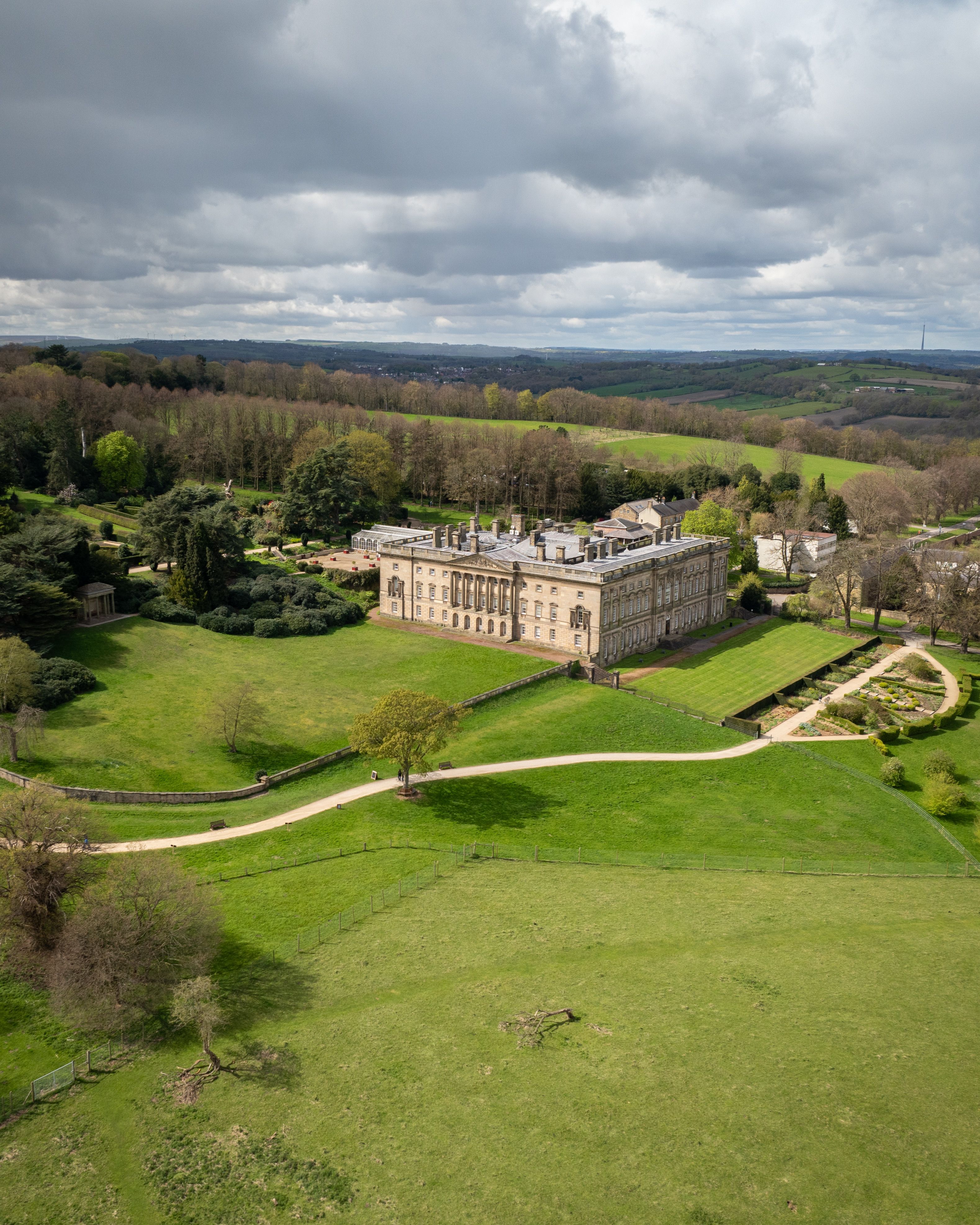 Aerial view of a country estate with a large historic house, formal gardens and extensive parkland.