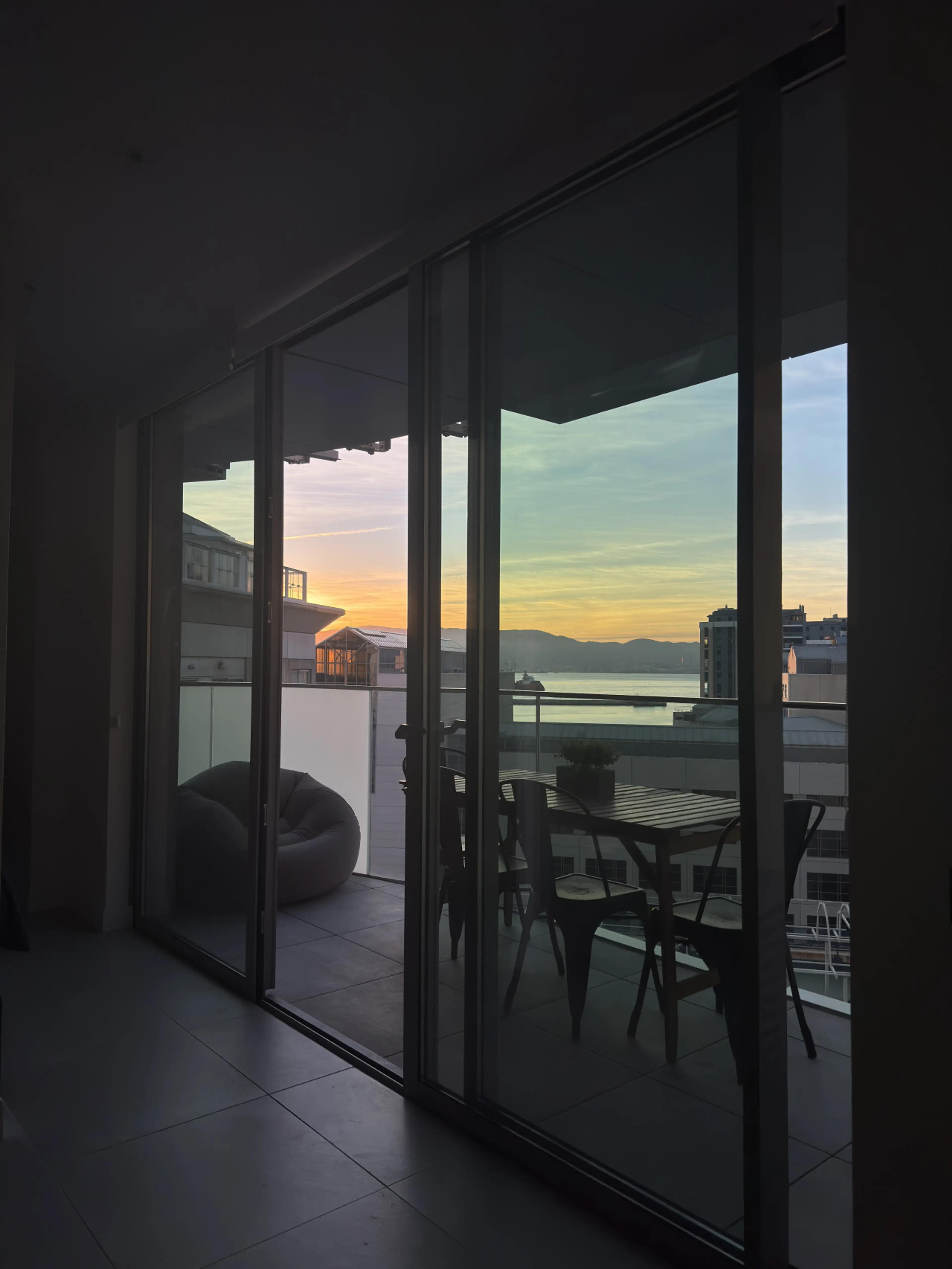 Sunset over the bay seen through the glass doors of an apartment balcony