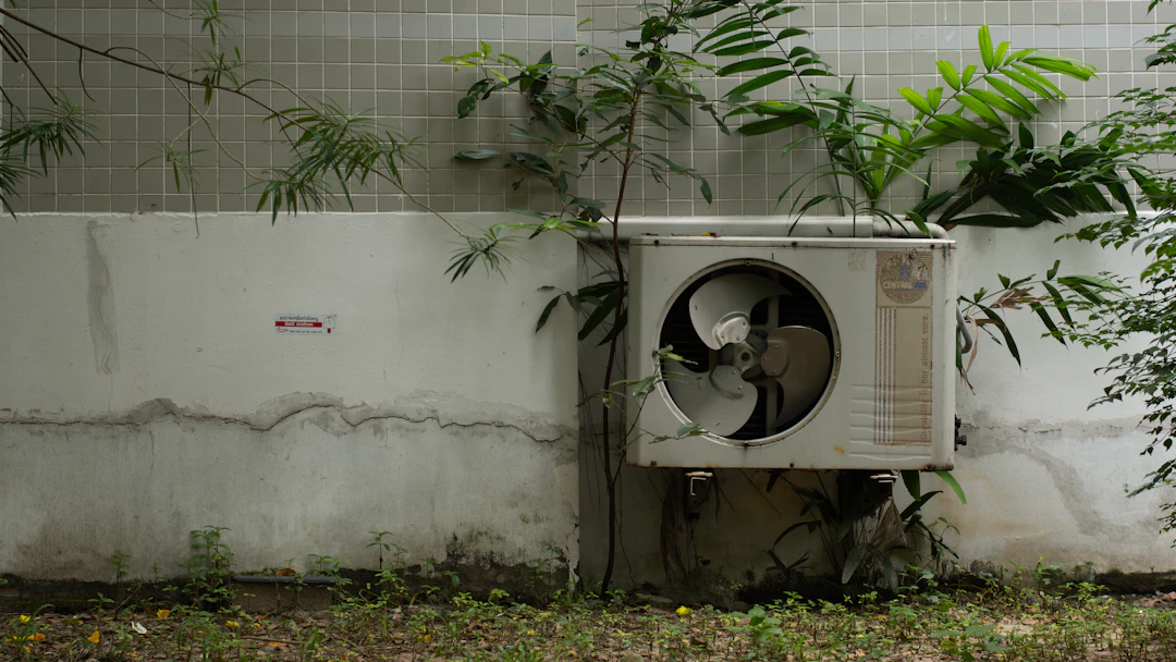 An outdoor air conditioning unit near some flowers.