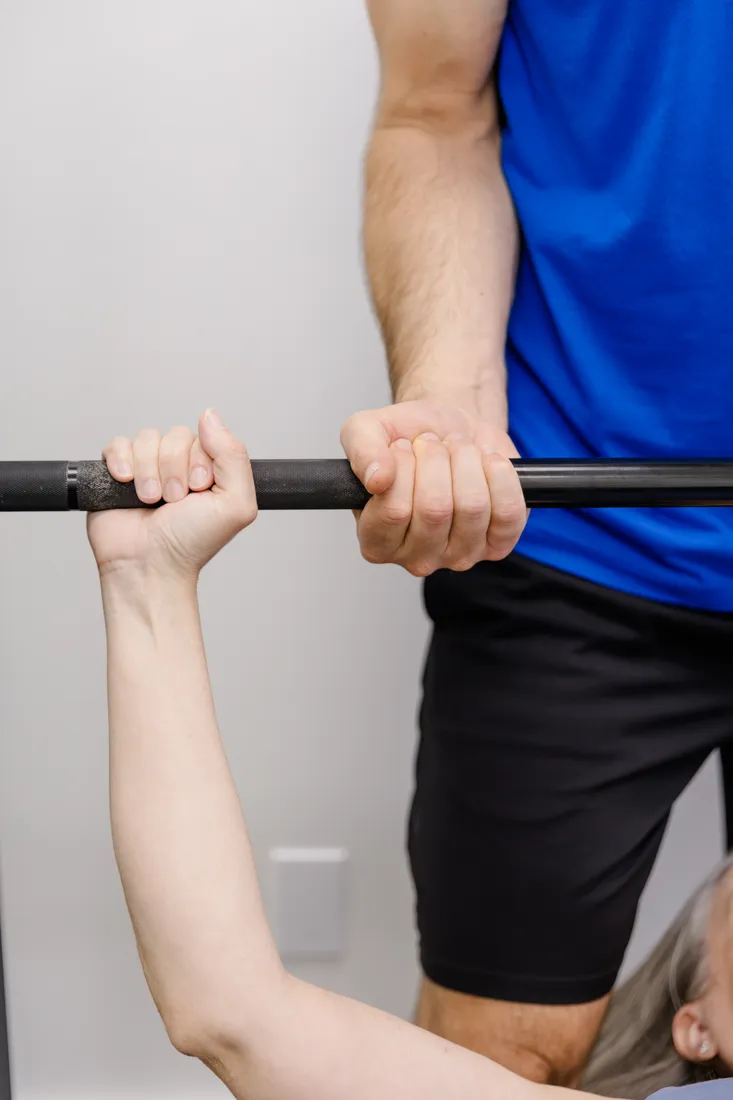 A patient's hands gripping a bar during strength work, with Matt Rieder, DPT, spotting at Renew Strength & Wellness in St. Augustine, FL