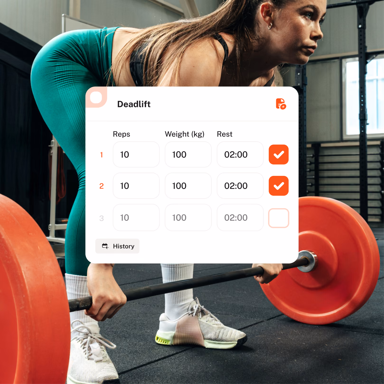 Person in light beige sweater and teal leggings stretching on a purple yoga mat indoors, with a smartphone placed on the mat displaying a workout app overlay showing a warm-up superset plan with reps, weight, and rest details.