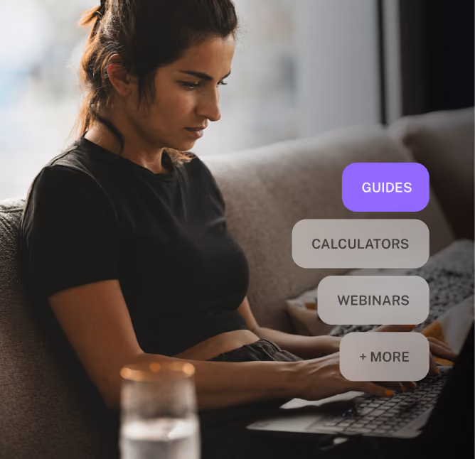 A focused woman with dark hair tied back, wearing a black shirt, sitting on a couch and typing on a laptop, with on-screen options labeled Guides, Calculators, Webinars, and + More.