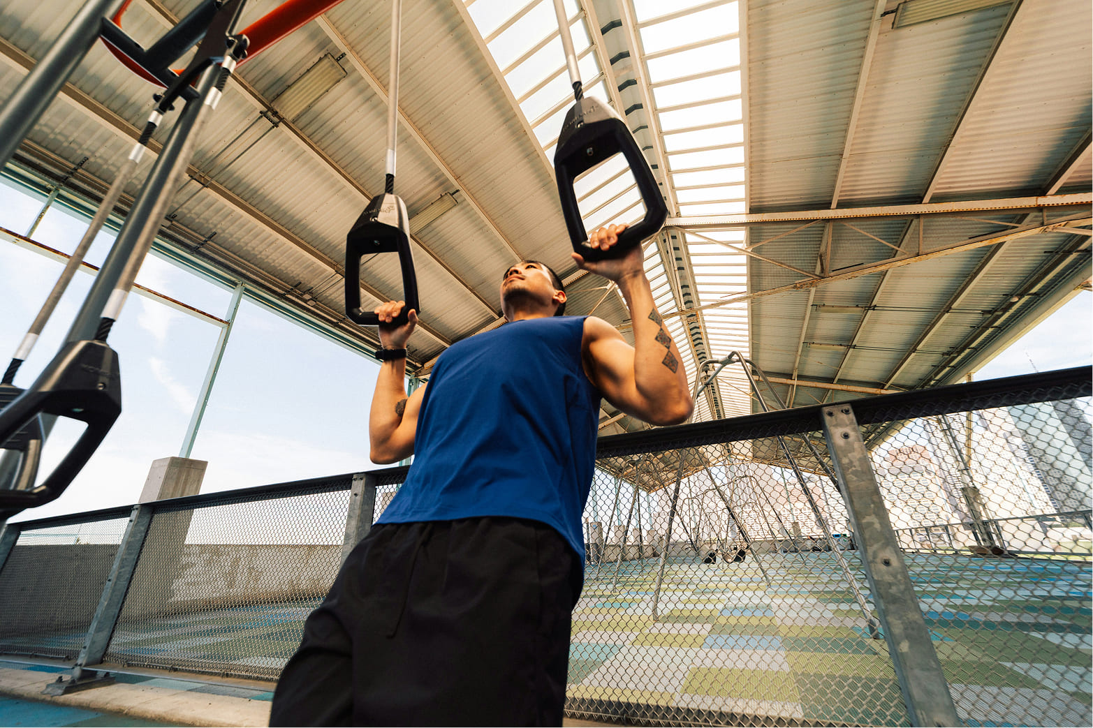 Man in a blue shirt, doing incline ring pull ups, in a public fitness area
