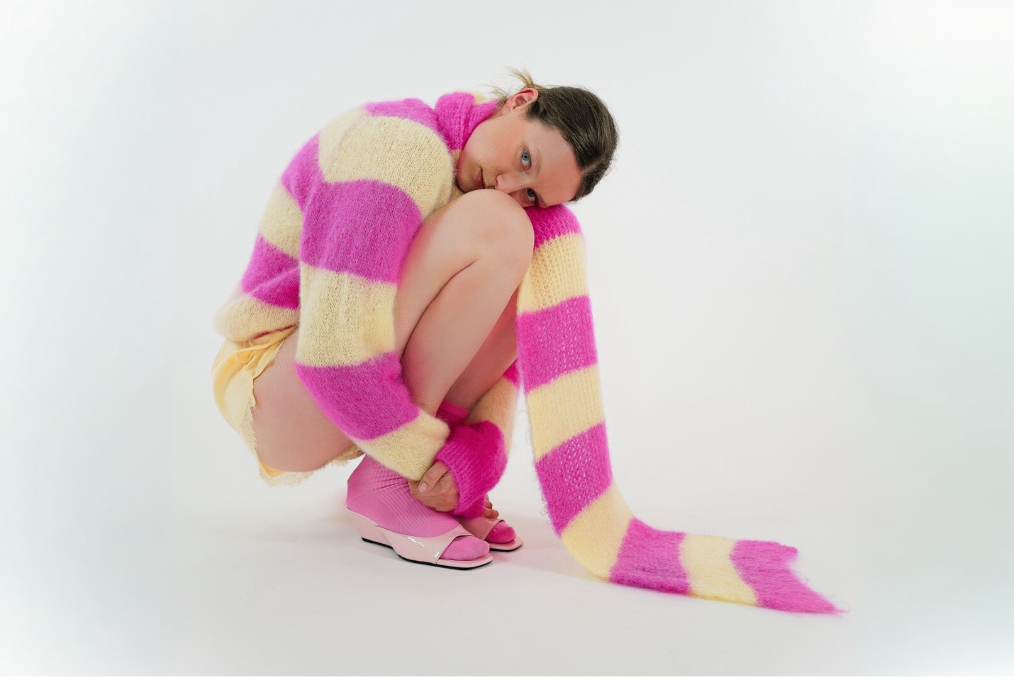 Model in a pink and cream striped mohair sweater and matching leg warmers from TWNS Original, crouched in a studio shot
