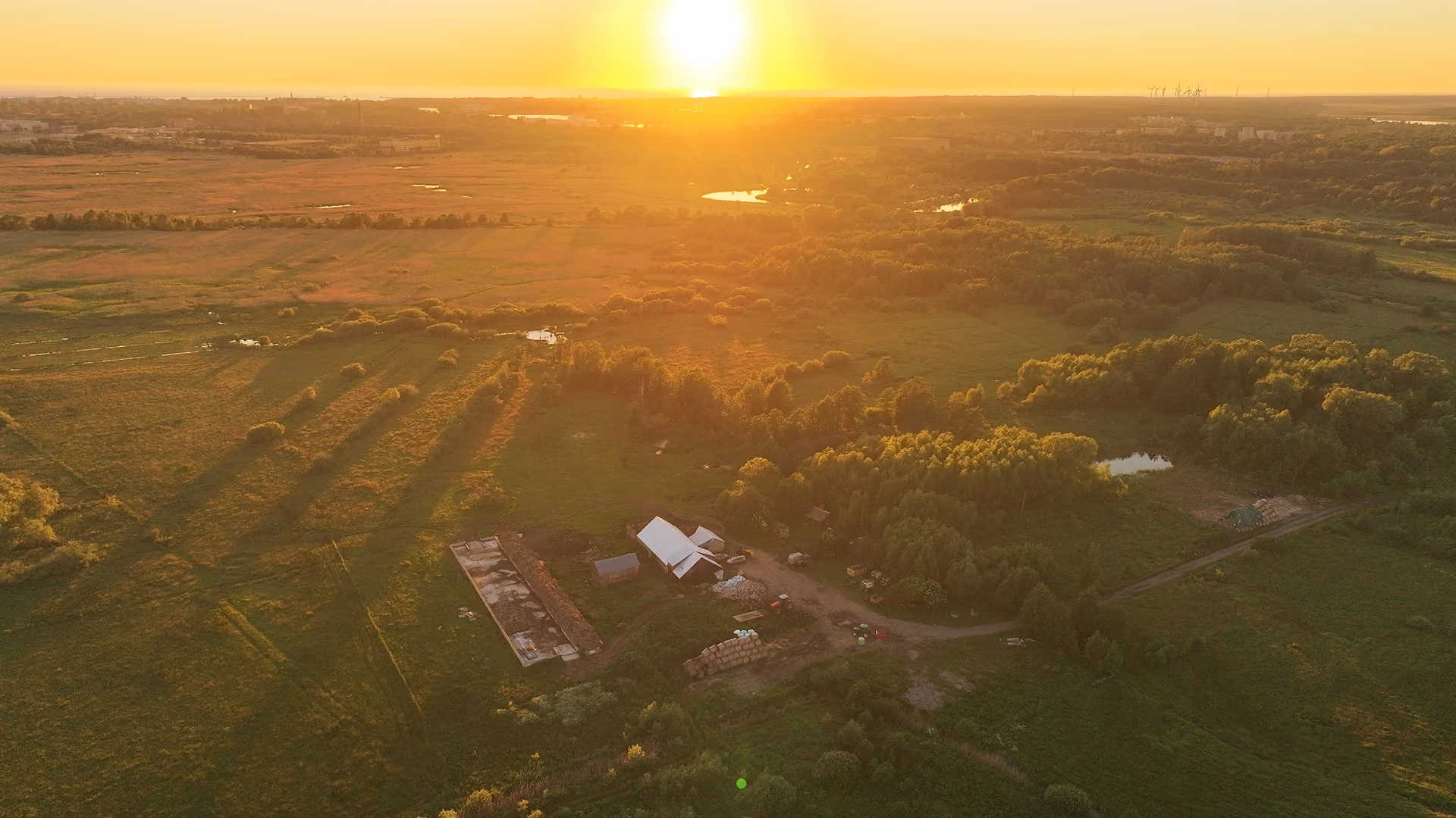 Aerial view of a farm and surrounding green fields at sunset with long tree shadows.