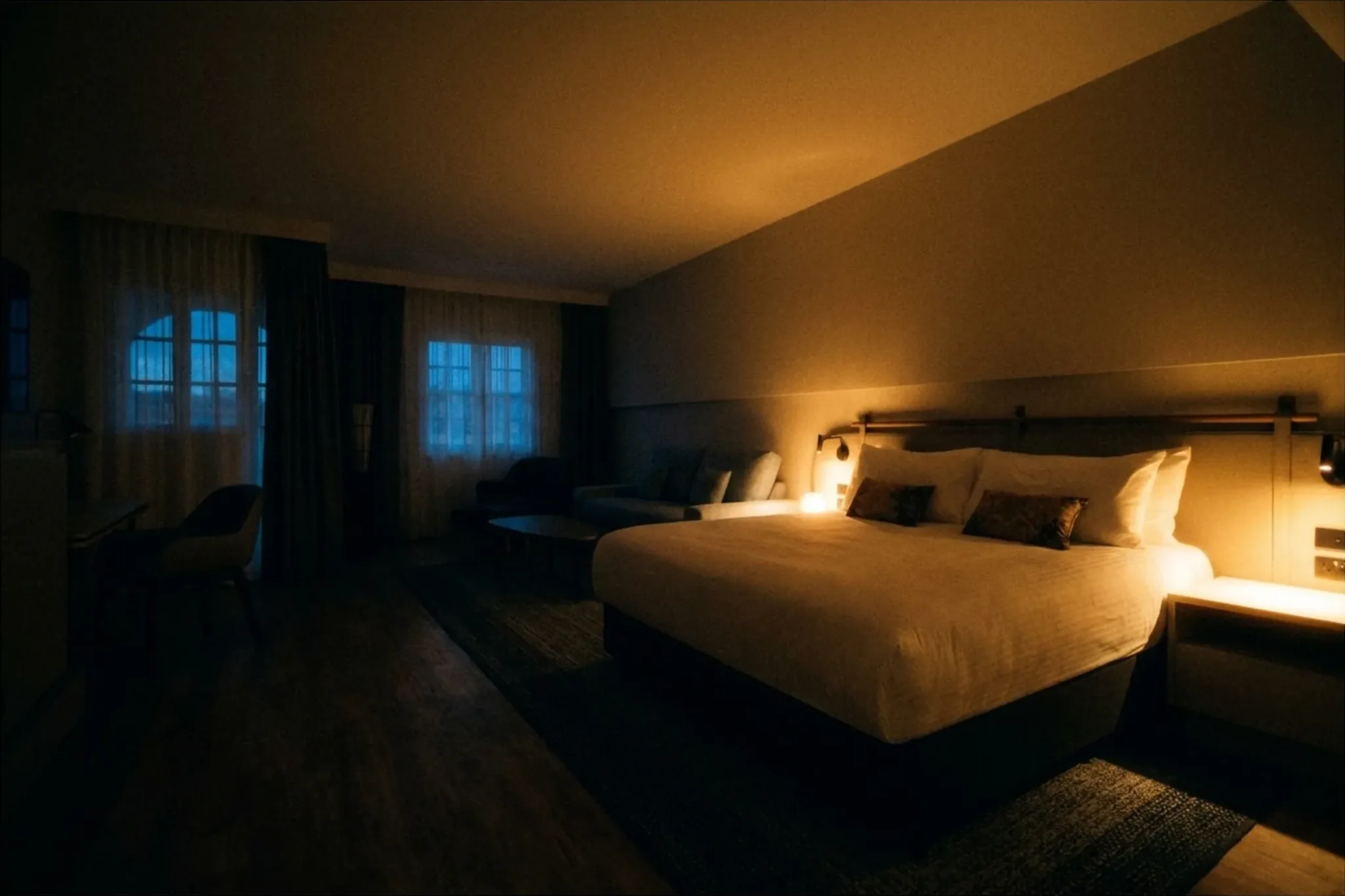 A guest room at dusk with a bedside lamp lit