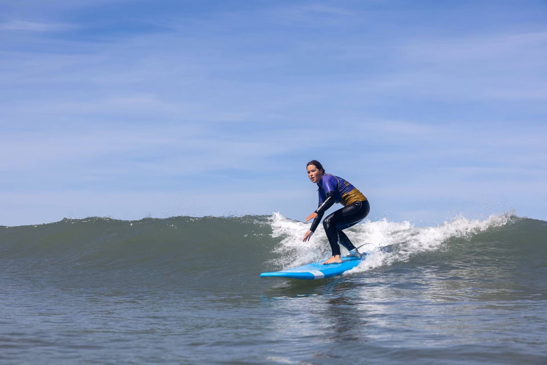 A person surfing on a light blue surfboard riding a small wave under a clear blue sky.