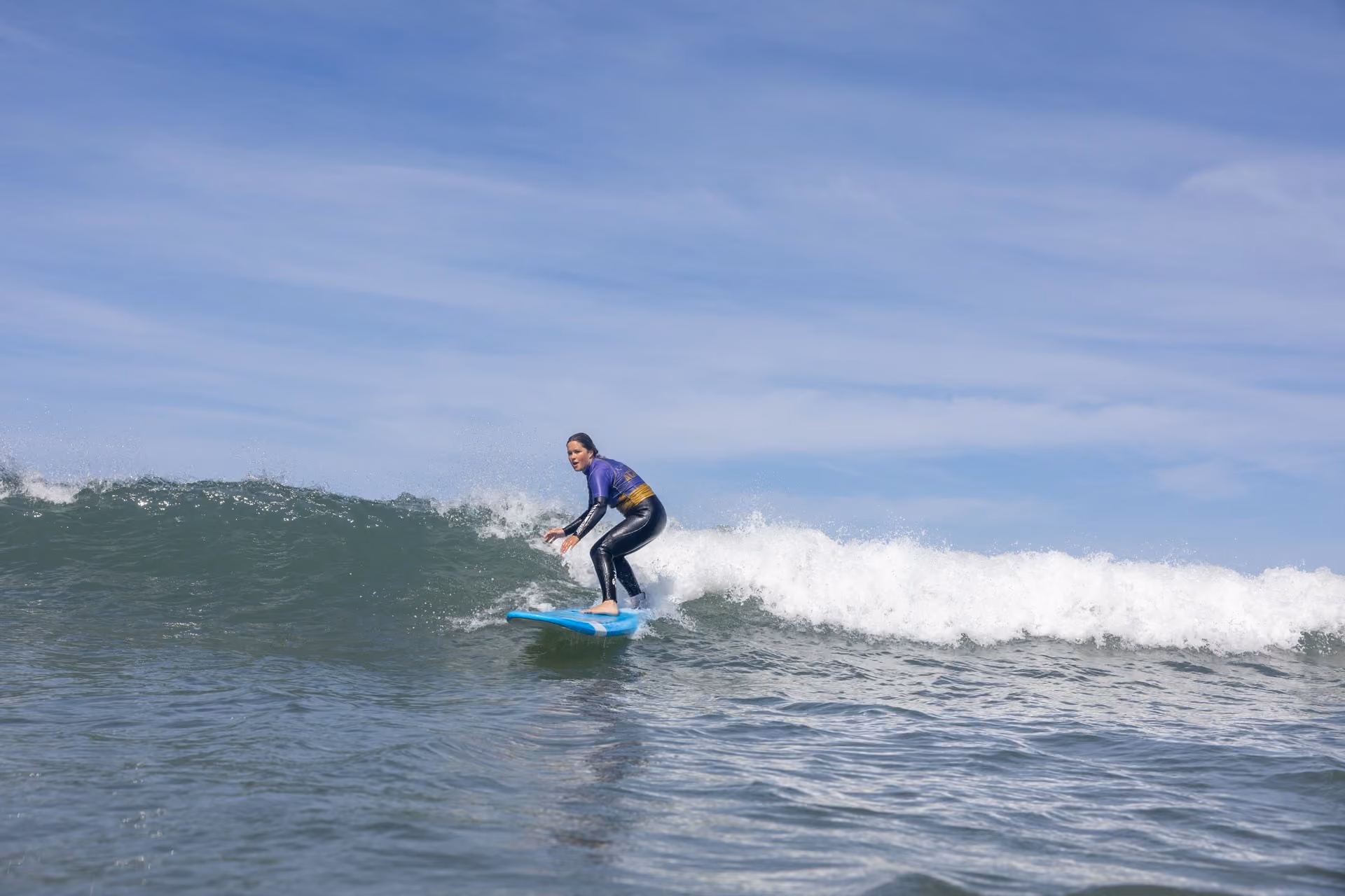 A person wearing a wetsuit surfing on a small wave in the ocean under a partly cloudy sky.