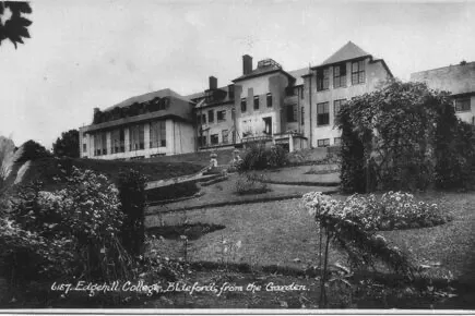 Black and white photo of Edgehill College in Bideford, showing a large multi-story building with many windows set behind a landscaped garden with bushes, trees, and flowerbeds.
