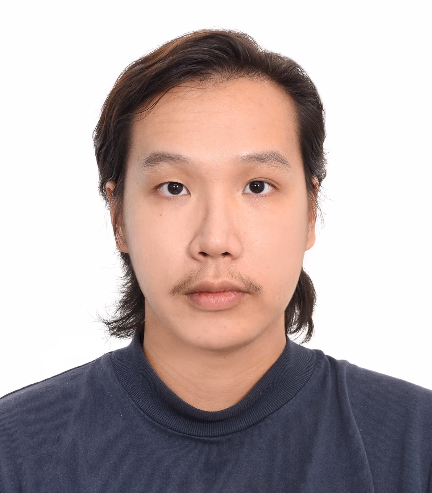 Portrait of a young man with medium-length dark hair, a thin mustache, and wearing a dark crew-neck shirt, looking directly at the camera against a plain white background.