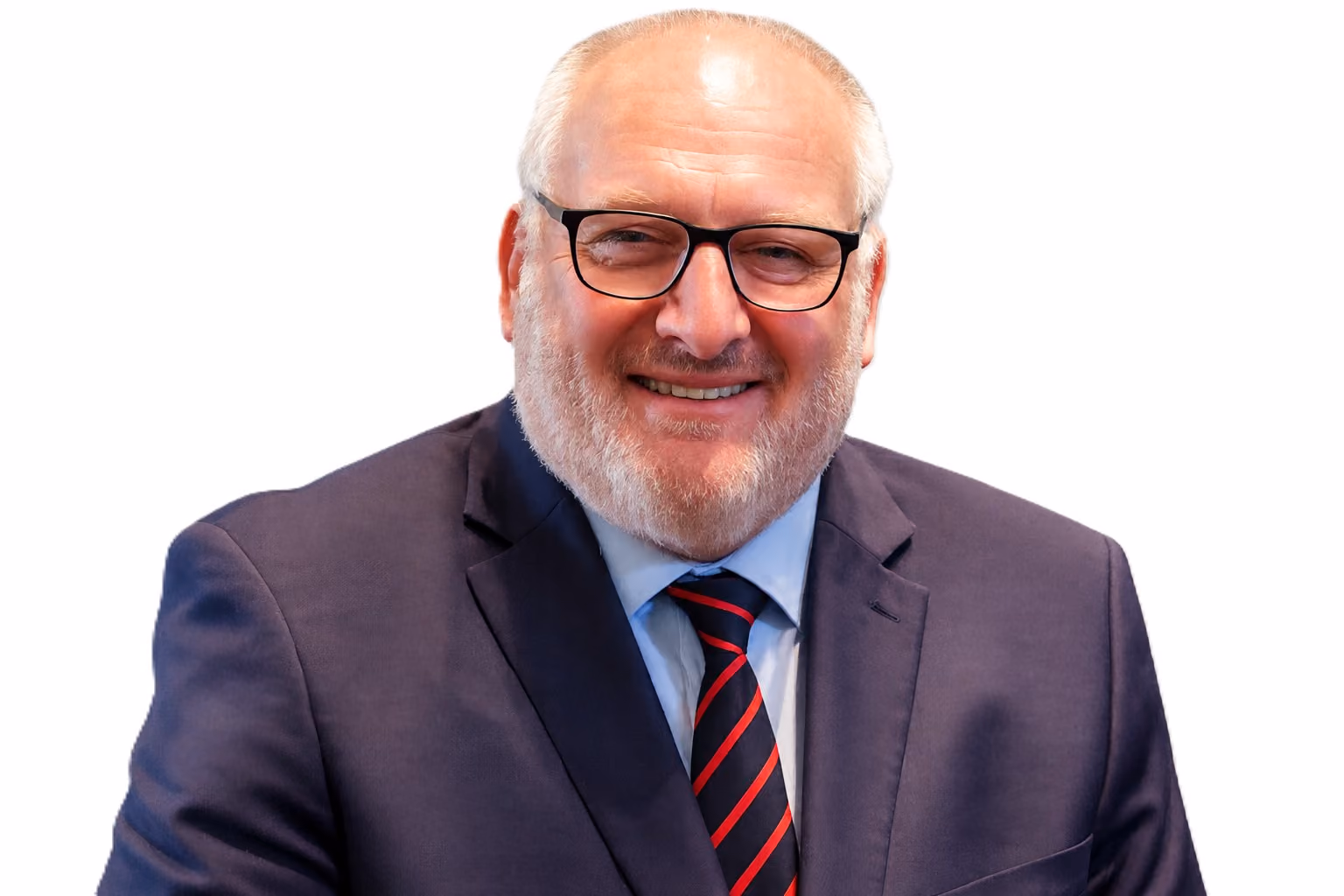 Smiling middle-aged man with light complexion, grey hair, and beard wearing black glasses, a dark suit jacket, light blue shirt, and navy tie with red stripes against a white background.